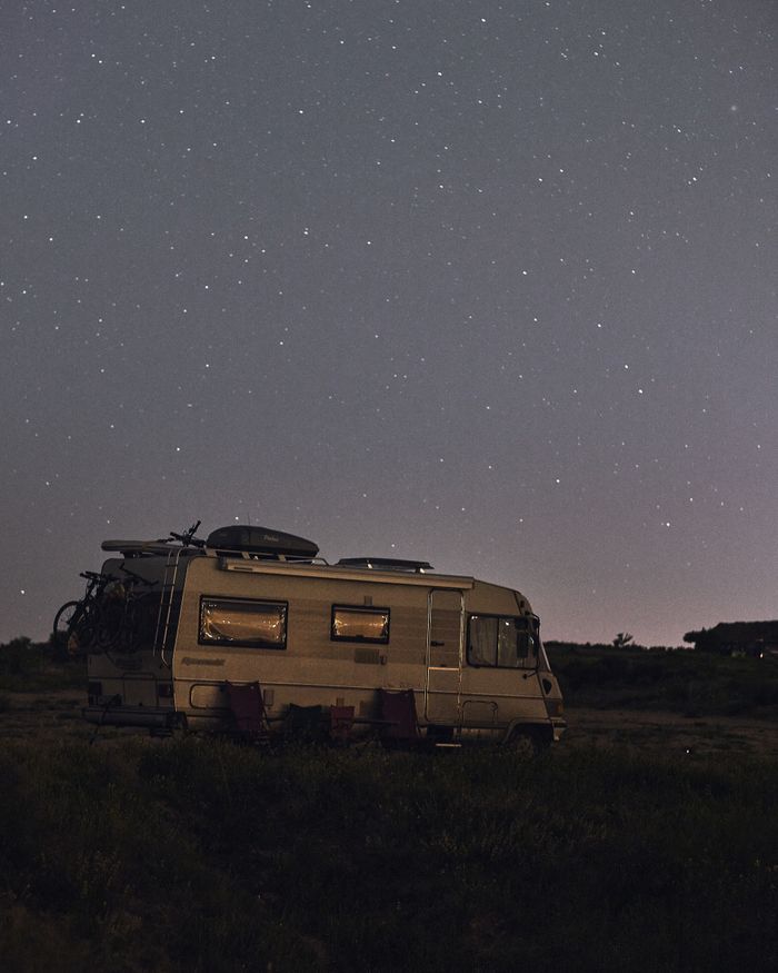 A serene night sky full of stars over a parked camper in a quiet wilderness setting.