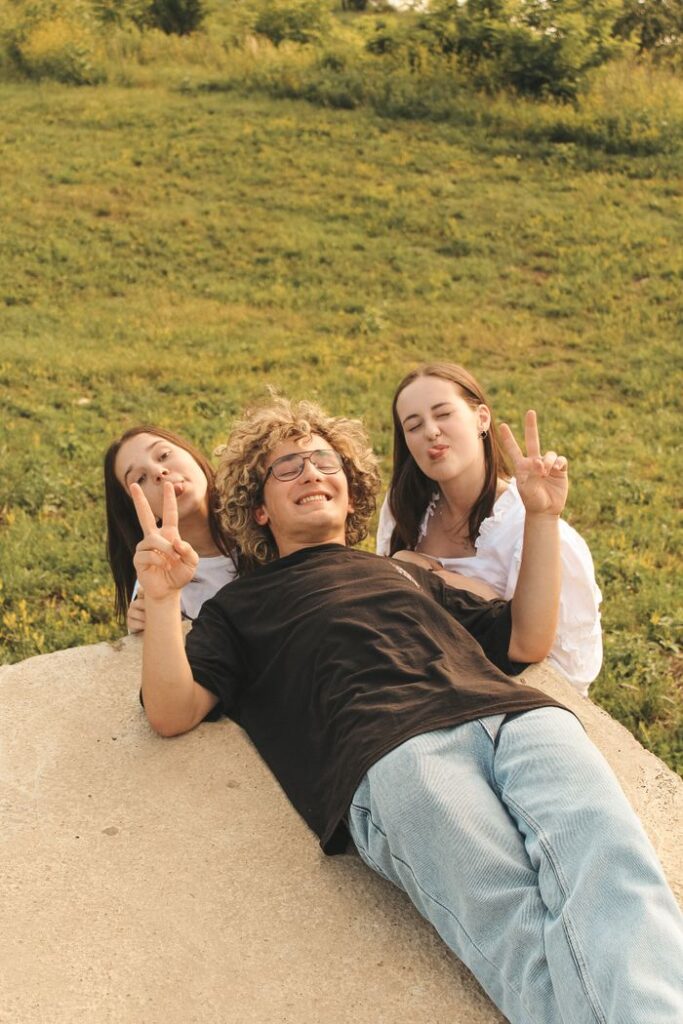 The Art of Drawing Readers In: Your attractive post title goes here Three young friends lie on the grass, smiling and posing with peace signs in a sunny park setting.